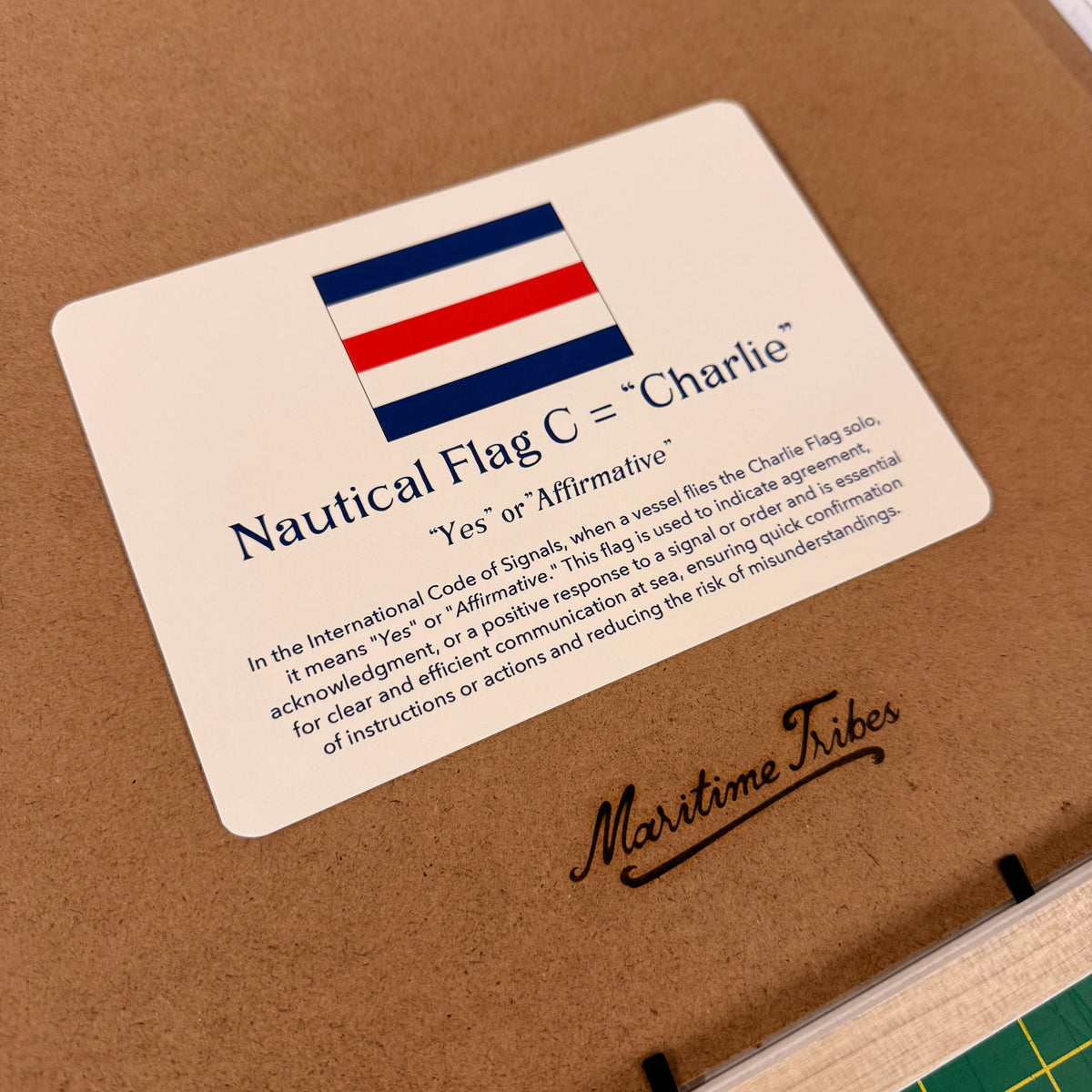 A close-up of a printed card labeled 'Nautical Fig C = "Chantie"' with a red, white, and blue striped flag graphic, placed on a brown surface next to a green cutting mat.