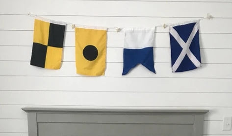 A gray wooden crib with a white and navy blue patterned blanket draped over the side, set in a nursery with a white shiplap wall, nautical flag bunting, and a white fluffy rug.